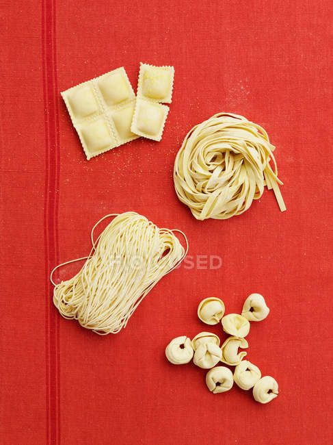 Свіжі сорти макаронних виробів на червоній скатертині — стокове фото