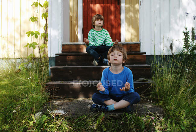 Два мальчика скрещивали ноги на ступеньках медитируя — стоковое фото