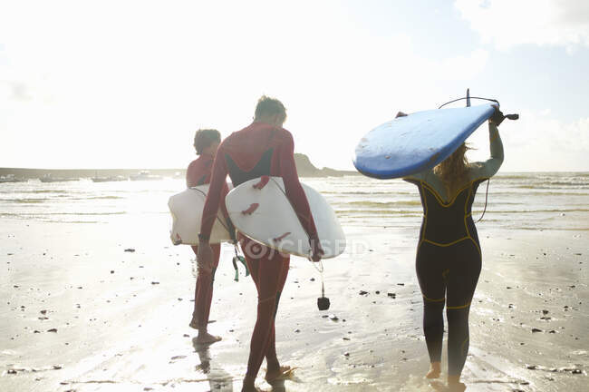 Groupe de surfeurs se dirigeant vers la mer, transportant des planches de surf, vue arrière — Photo de stock