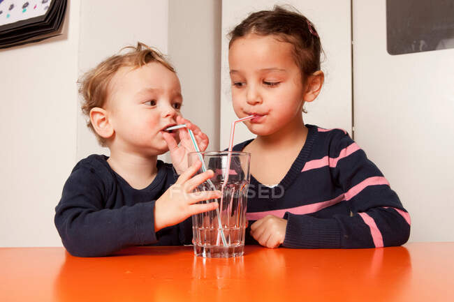 Niño y niña bebiendo agua con pajitas - foto de stock