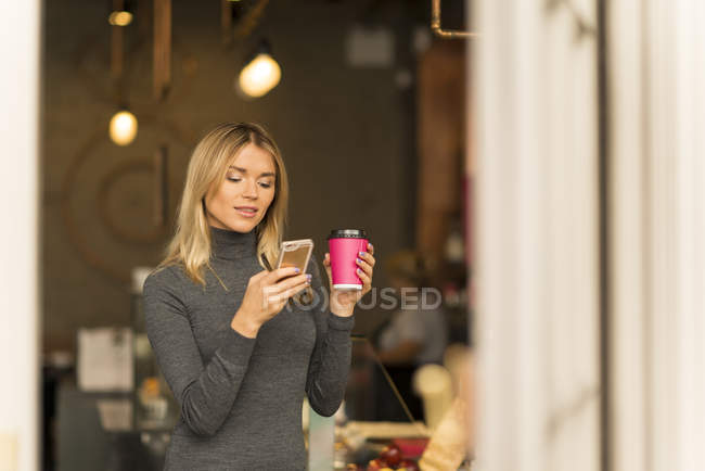 Mujer con café para llevar usando smartphone - foto de stock