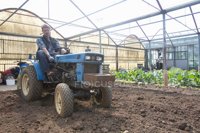 Biobauer auf Traktor pflegt Boden im Polytunnel — Stockfoto