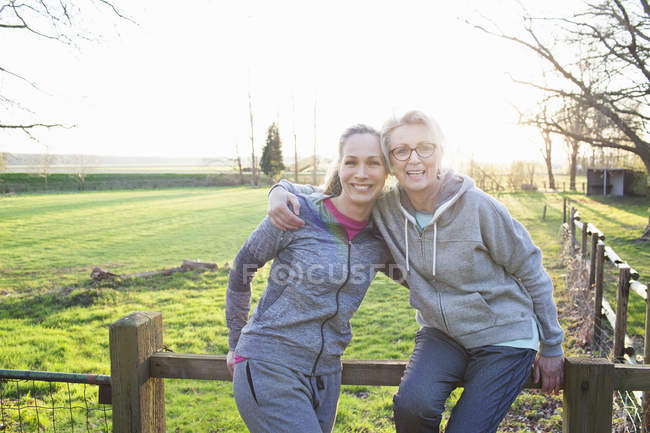Mulheres vestindo roupas esportivas encostadas à cerca olhando para a câmera abraçando e sorrindo — Fotografia de Stock