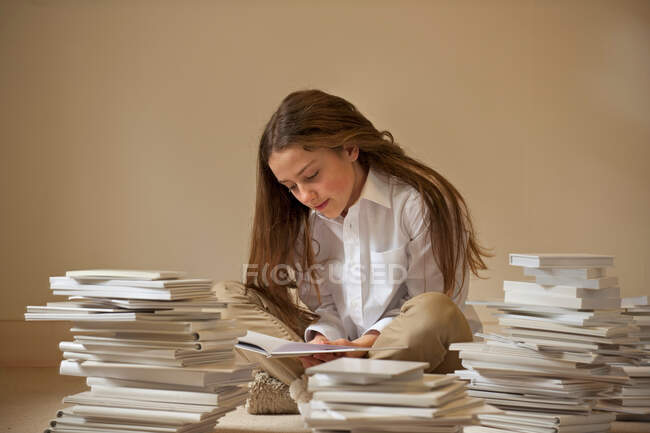 Дівчина сидить на підлозі читання в оточенні купи книг — стокове фото