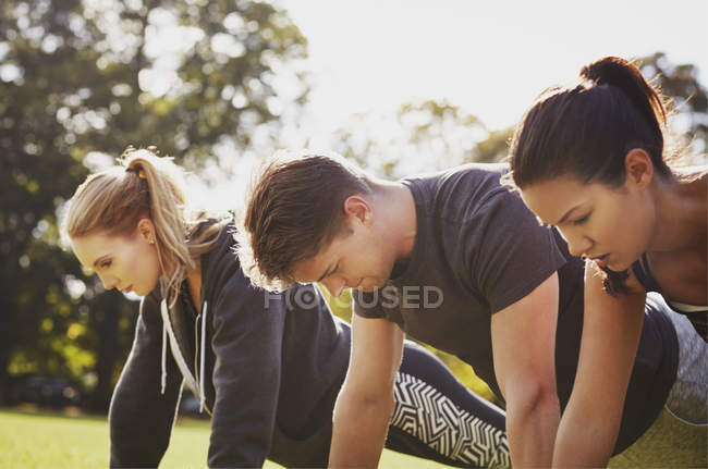 Homem e duas mulheres fazendo empurrar para cima formação no parque — Fotografia de Stock