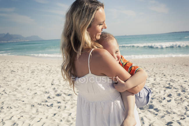 Mãe carregando jovem filho na praia — Fotografia de Stock