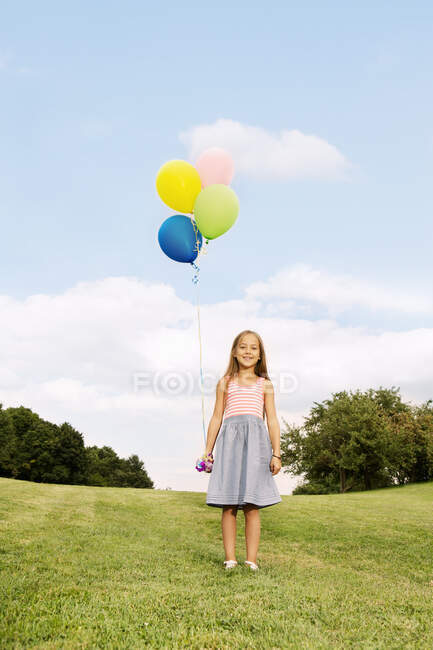 Girl holding balloons standing on grass — Stock Photo