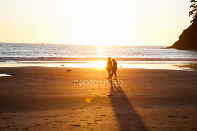 Дві жінки, що ходять на пляжі на заході сонця, вибірковий фокус — стокове фото