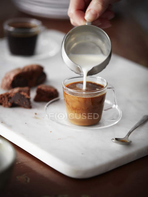 Imagen recortada de la mujer vertiendo leche en la taza de café - foto de stock