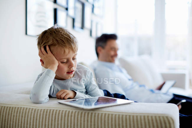 Père et fils assis sur le canapé et utilisant des tablettes numériques — Photo de stock