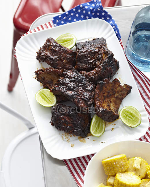 Plate of barbecued ribs with lime and corn cobs — Stock Photo