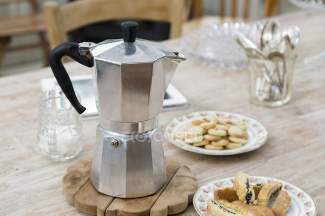 Stove top coffee pot with plates of baked good on dining table — Stock Photo