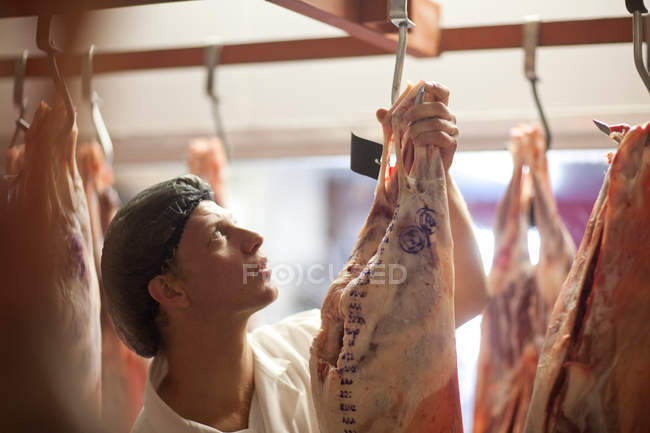 Giovane macellaio maschio che ispeziona la carne — Foto stock