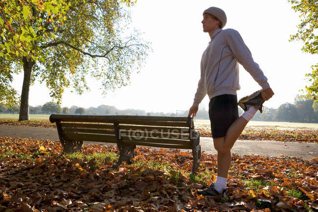 Young man stretching by bench — Stock Photo