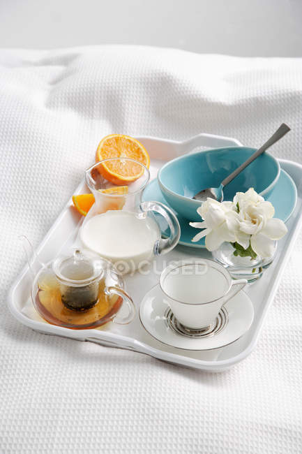Frühstückstablett mit Tee, Milch und Orange auf dem Bett — Stockfoto