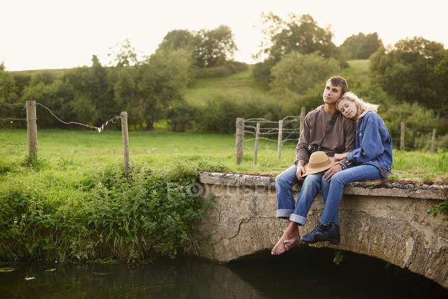 Романтична молода пара сидить на річковому пішохідному мосту — стокове фото