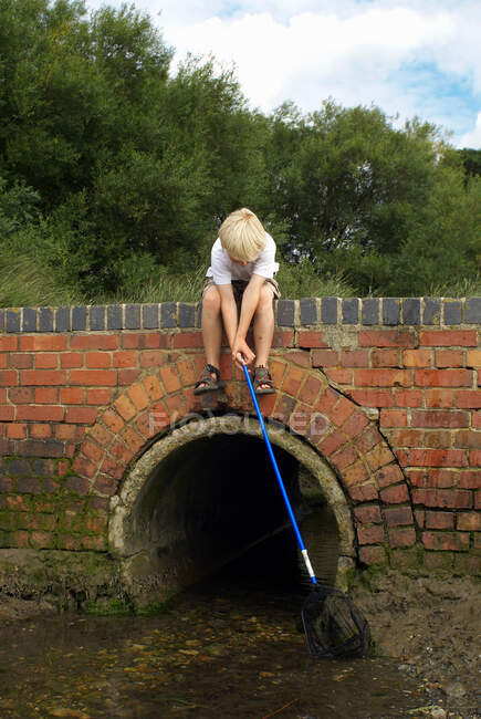 Мальчик рыбачит с сеткой с моста — стоковое фото