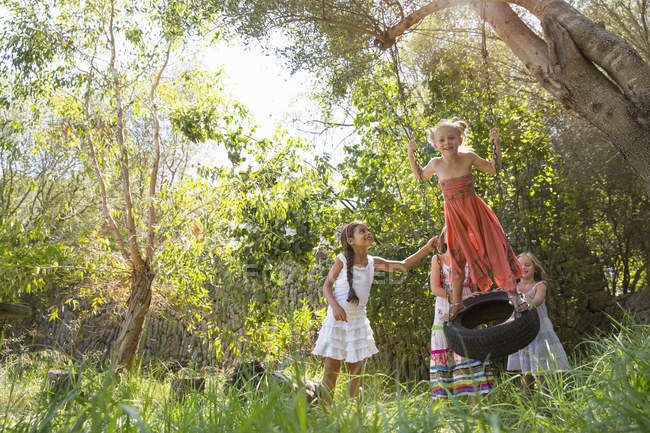Quatro meninas brincando no balanço pneu árvore no jardim — Fotografia de Stock