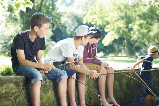 Niños sentados en la pared y pescando en el estanque - foto de stock