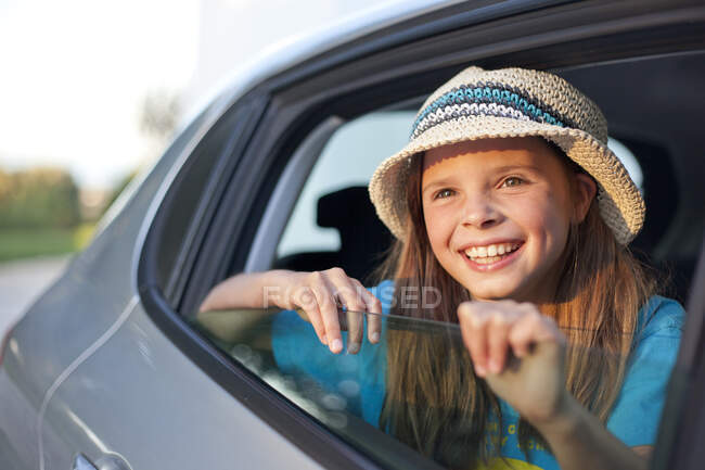 Menina usando chapéu olhando através da janela do carro aberto, sorrindo — Fotografia de Stock