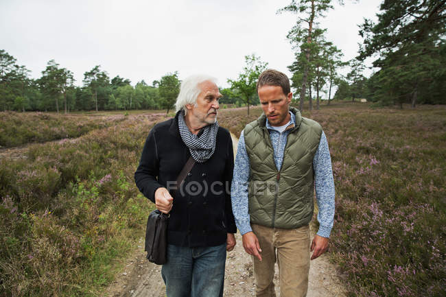 Отец и взрослый сын идут по грунтовой дорожке — стоковое фото