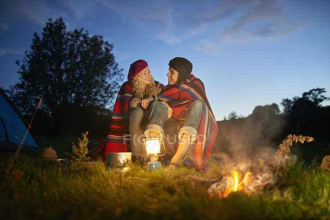 Giovane coppia di campeggio seduto vicino al falò al tramonto — Foto stock