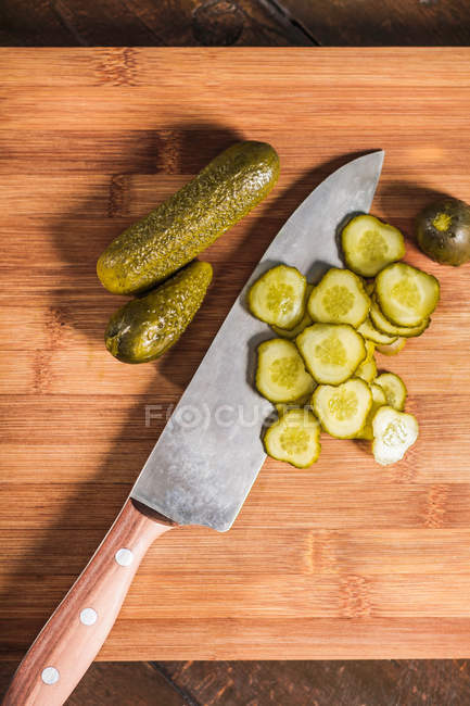Knife with chopped pickles on wooden board — Stock Photo