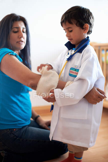 Мальчик, одетый как доктор, накладывающий повязку на женщину — стоковое фото