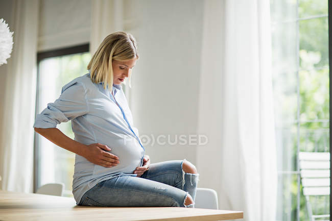 Embarazo término completo mujer joven sentada en la mesa de la cocina - foto de stock