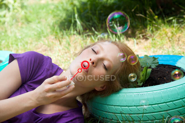 Mulher deitada no pneu soprando bolhas — Fotografia de Stock