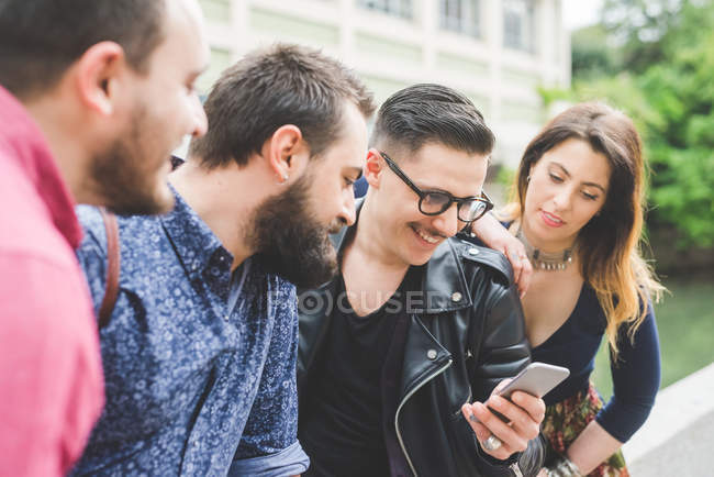 Grupo de amigos mirando el mensaje en el teléfono celular juntos - foto de stock
