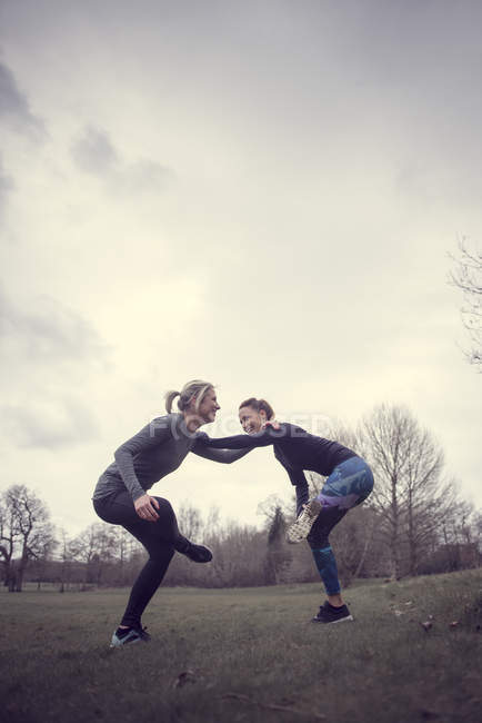 Frauen in Feldhänden auf den Schultern, auf einem Bein balancierend lächelnd — Stockfoto