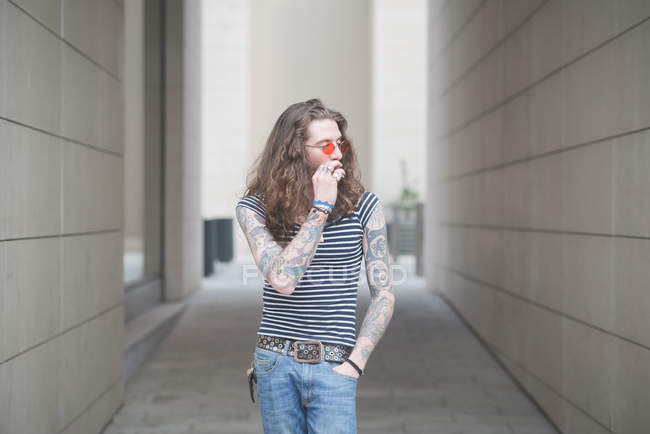Young male hippy smoking cigarette in city alley — Stock Photo