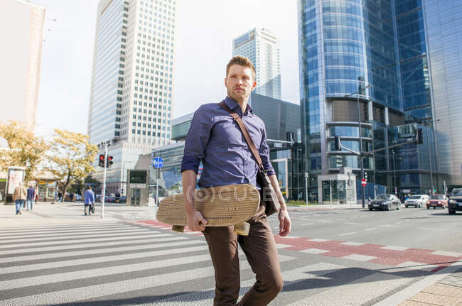 Uomo d'affari casuale attraversamento della strada in possesso di skateboard — Foto stock