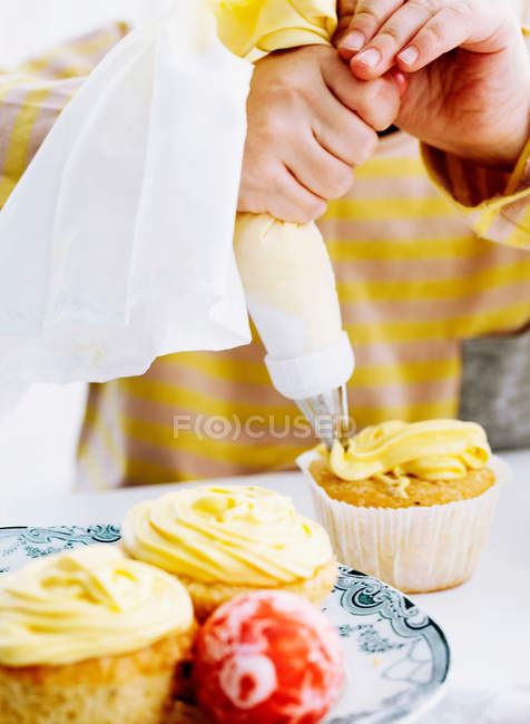 Hands icing cupcake on table, cropped shot — Stock Photo