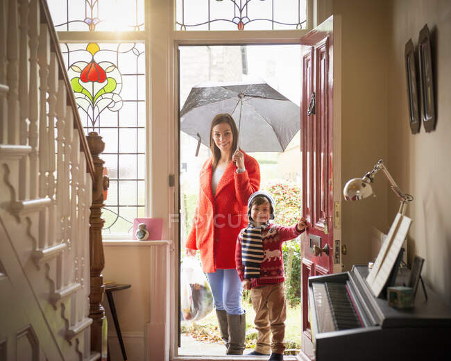 Madre e hijo que llegan a la puerta principal del hogar en el día lluvioso, retrato - foto de stock