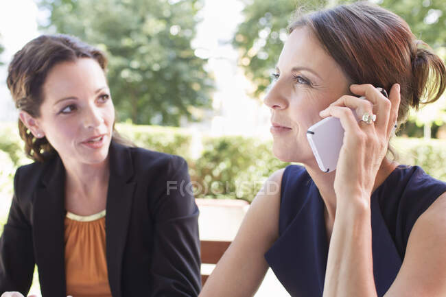 Two mature female friends chatting on smartphone in garden — Stock Photo