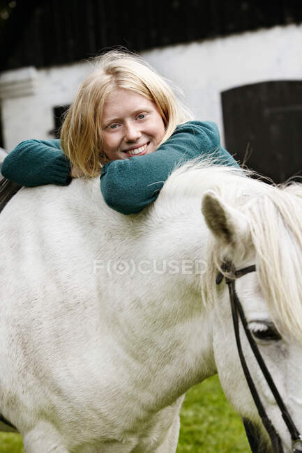 Girl hugging white horse outdoors — Stock Photo