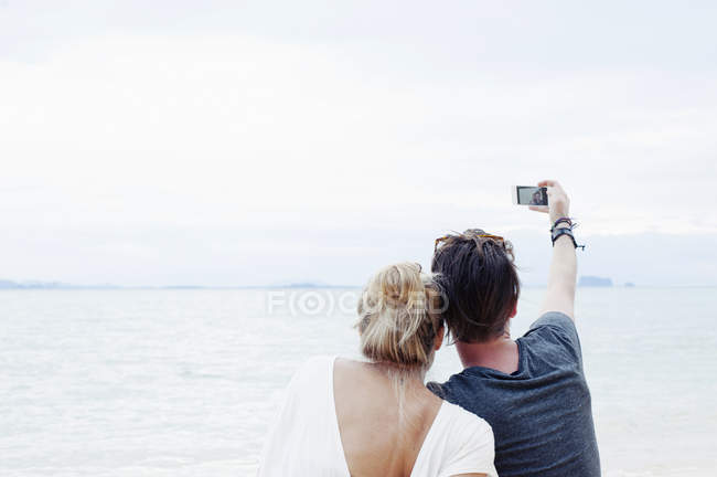 Visão traseira do jovem casal levando selfie smartphone na praia, Kradan, Tailândia — Fotografia de Stock