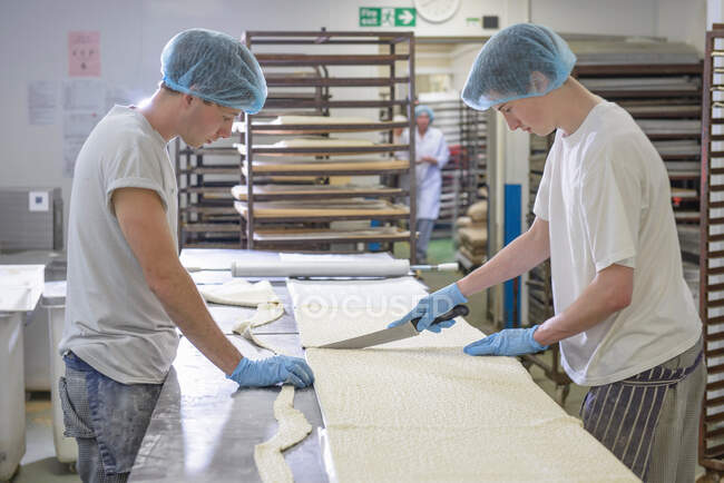 Cozinheiros em vestuário de proteção preparando comprimento da massa — Fotografia de Stock