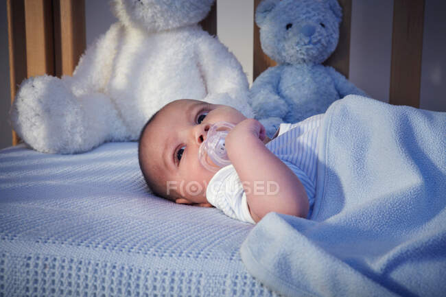 Bébé garçon et ours en peluche dans la crèche la nuit — Photo de stock
