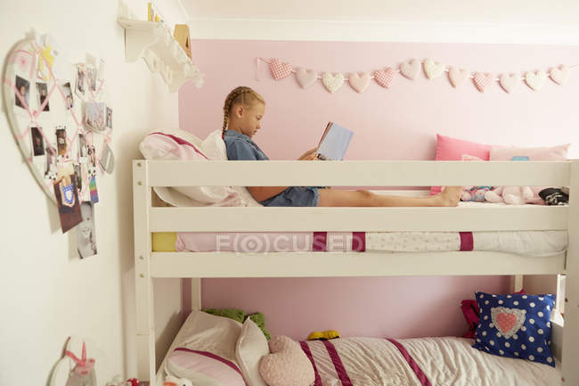 Vista laterale della ragazza seduta sulla parte superiore del letto a castello lettura rivista — Foto stock