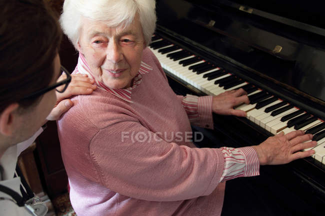 Médecin regardant femme plus âgée jouer du piano — Photo de stock
