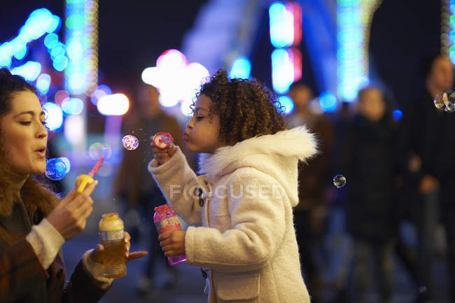 Mother and daughter blowing bubbles, at funfair — Stock Photo