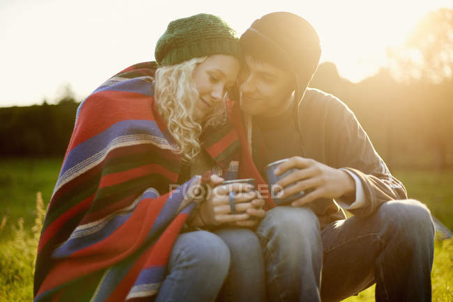 Romántica joven pareja de camping envuelta en manta con bebidas de té - foto de stock