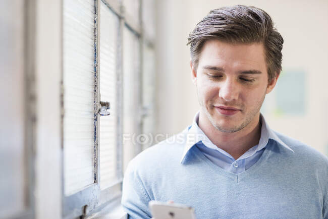 Joven hombre de negocios mensajes de texto en el teléfono inteligente en la oficina - foto de stock