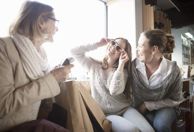 Familia femenina de tres generaciones probándose gafas de sol en la tienda - foto de stock
