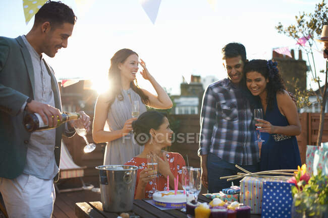Друзья на вечеринке на террасе на крыше наливают шампанское — стоковое фото