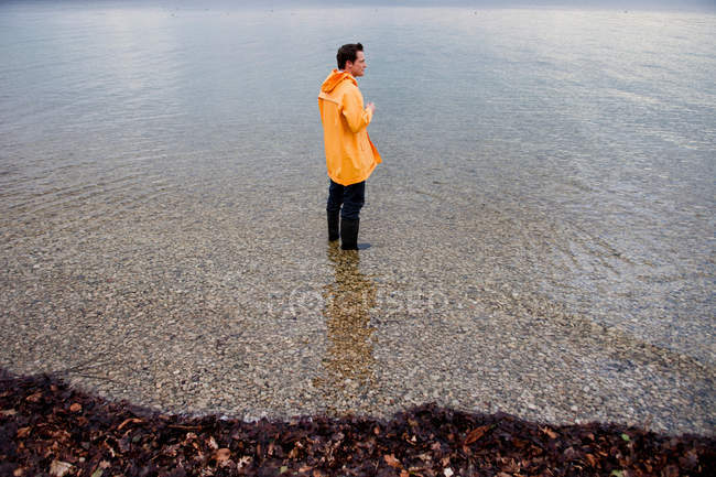 Homme dans un manteau de pluie en eau peu profonde — Photo de stock