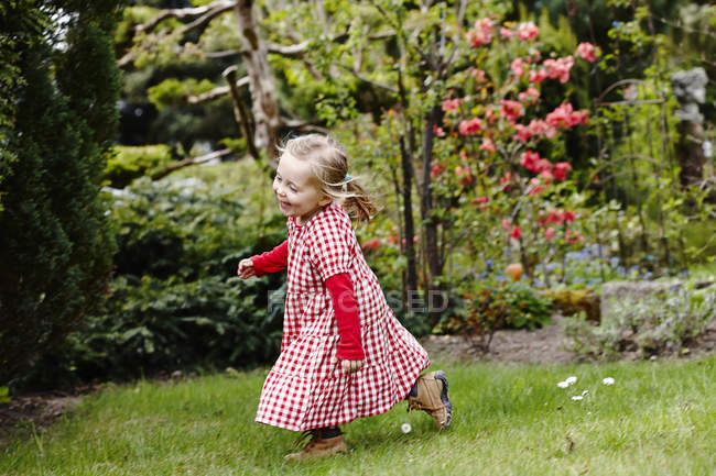 Kleines Mädchen in kariertem Kleid läuft durch Garten — Stockfoto